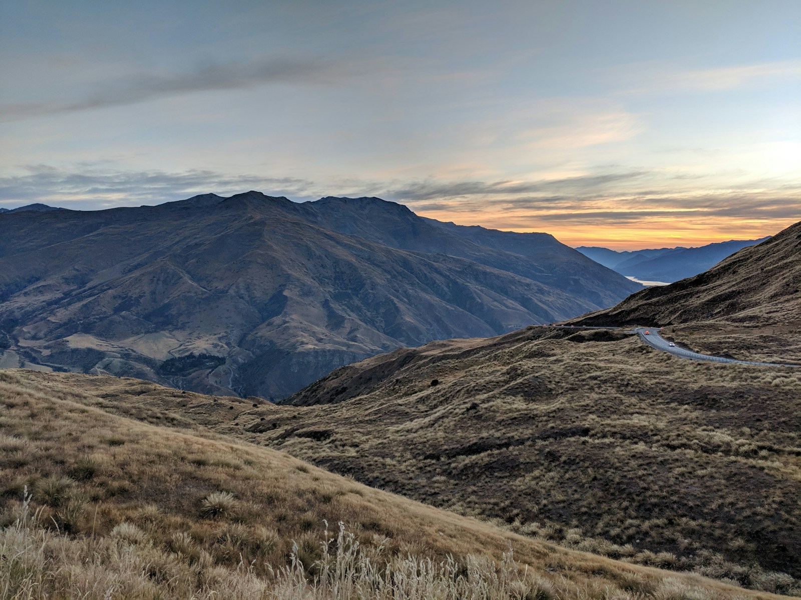Crown Range road winding through golden tussock hills into Queenstown - campervan road trip New Zealand